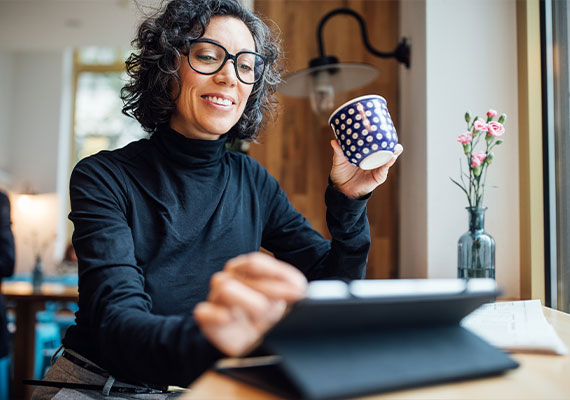 Woman drinking coffee while working on her tablet and smiling