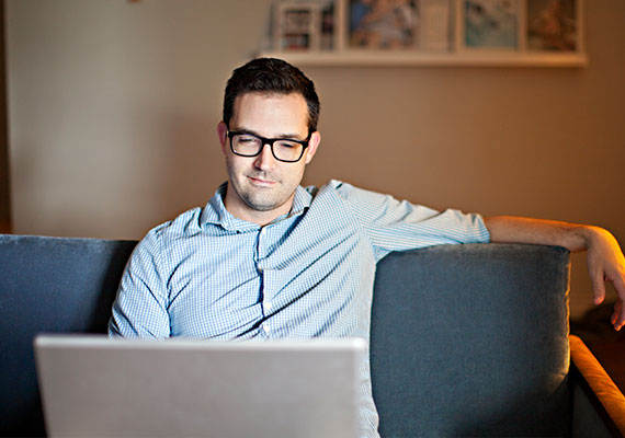 Man working on his laptop sitting on a couch and smiling